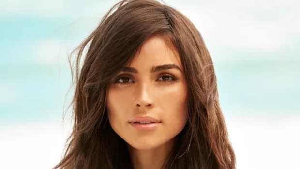 Olivia Culpo stands before the ocean and poses for the camera.